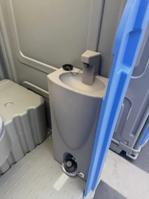 Inside a porta potty with a built-in hand sink and soap