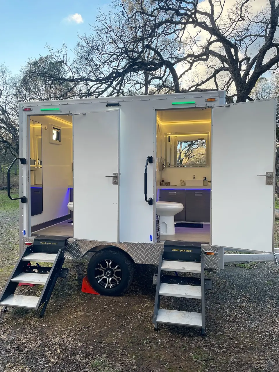 Restroom trailer with lit interior and fold-down steps at an evening event