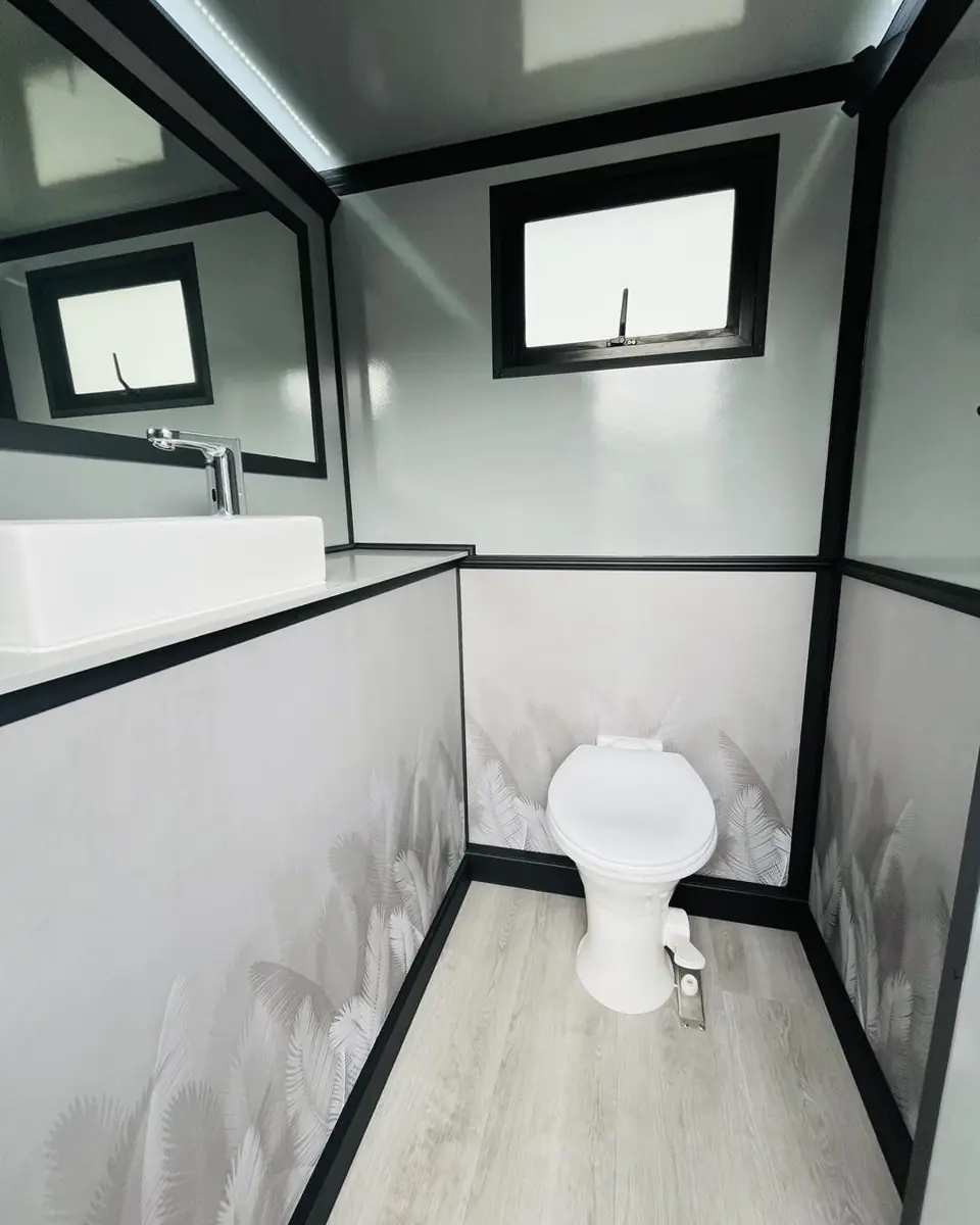 Clean restroom trailer stall with toilet, window and wood-look floor