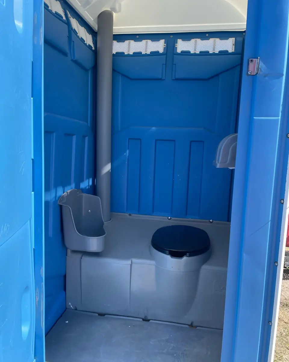 Inside a standard porta potty showing the seat, urinal and vent pipe