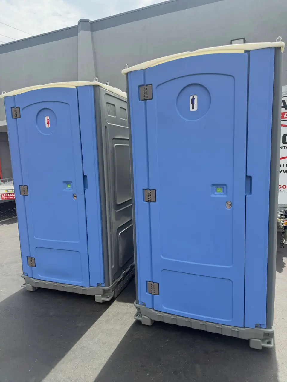 Two blue porta potties side by side on a paved lot